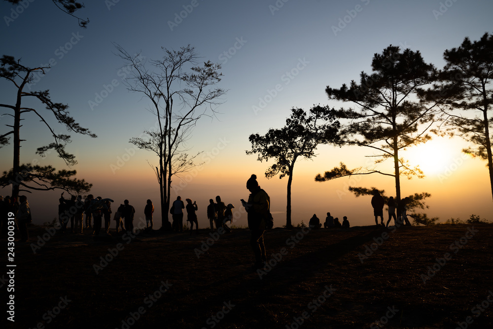 Image of sunrise on orange and yellow horizon with people's silhouette surrounded by pine trees ( Phu kradueng Thailand )