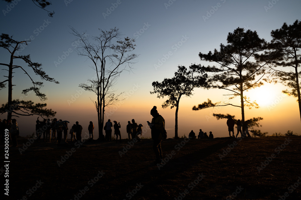 Image of sunrise on orange and yellow horizon with people's silhouette surrounded by pine trees ( Phu kradueng Thailand ) Image of sunrise on orange and yellow horizon with people's silhouette surrounded by pine trees ( Phu kradueng Thailand )