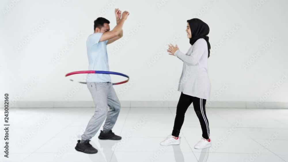 Funny young man exercising with hula hoop while his wife giving support and applause at home. Shot in 4k resolution Funny young man exercising with hula hoop while his wife giving support and applause at home. Shot in 4k resolution