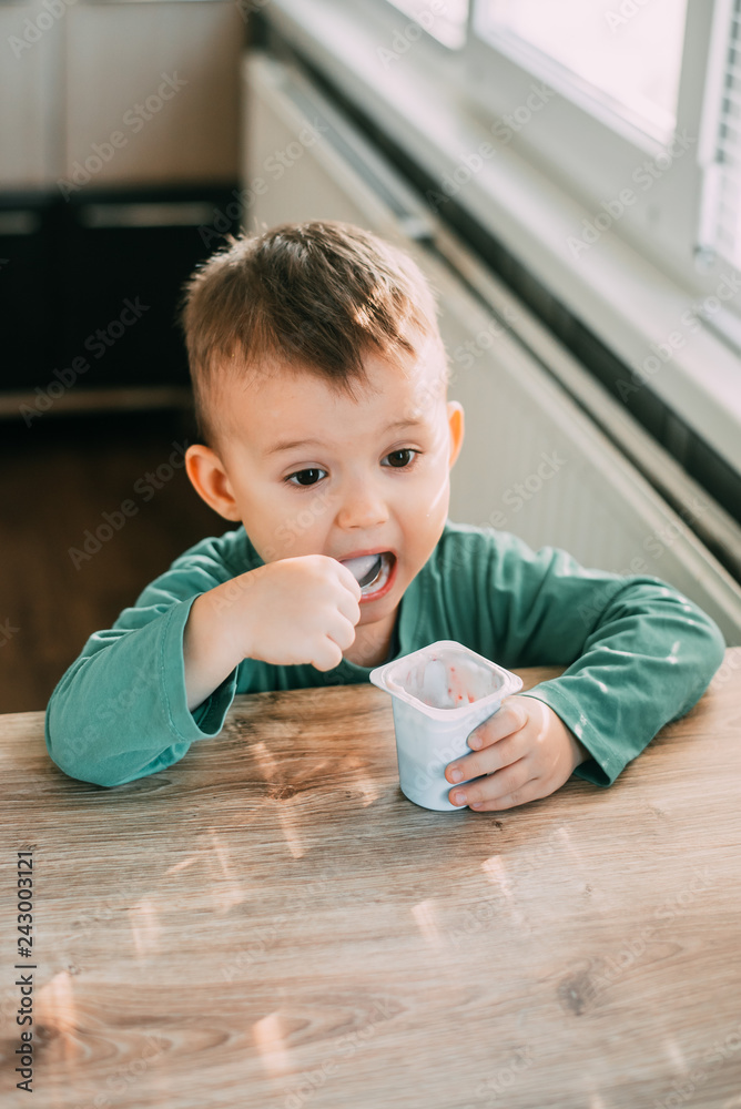 child eating yogurt in the kitchen in a green jacket, daylight child eating yogurt in the kitchen in a green jacket, daylight