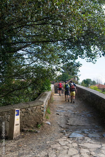 FURELOS, SPAIN - JULY 31, 2016: Some young pilgrims with backpacks cross a medieval bridge, making the Camino de Santiago. photo