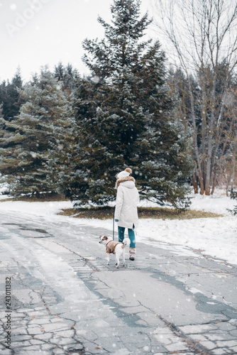Active winter leisure - woman walking with dog in snowy park. Instagram style photo.