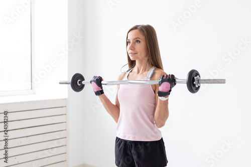 Sport, fitness and people concept - Fit young woman exercises with a weight bar, doing her biceps