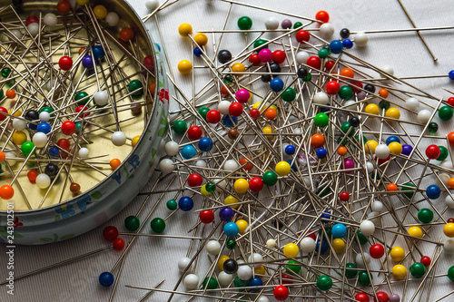 A tin of sewing pins and some loose on the table photo