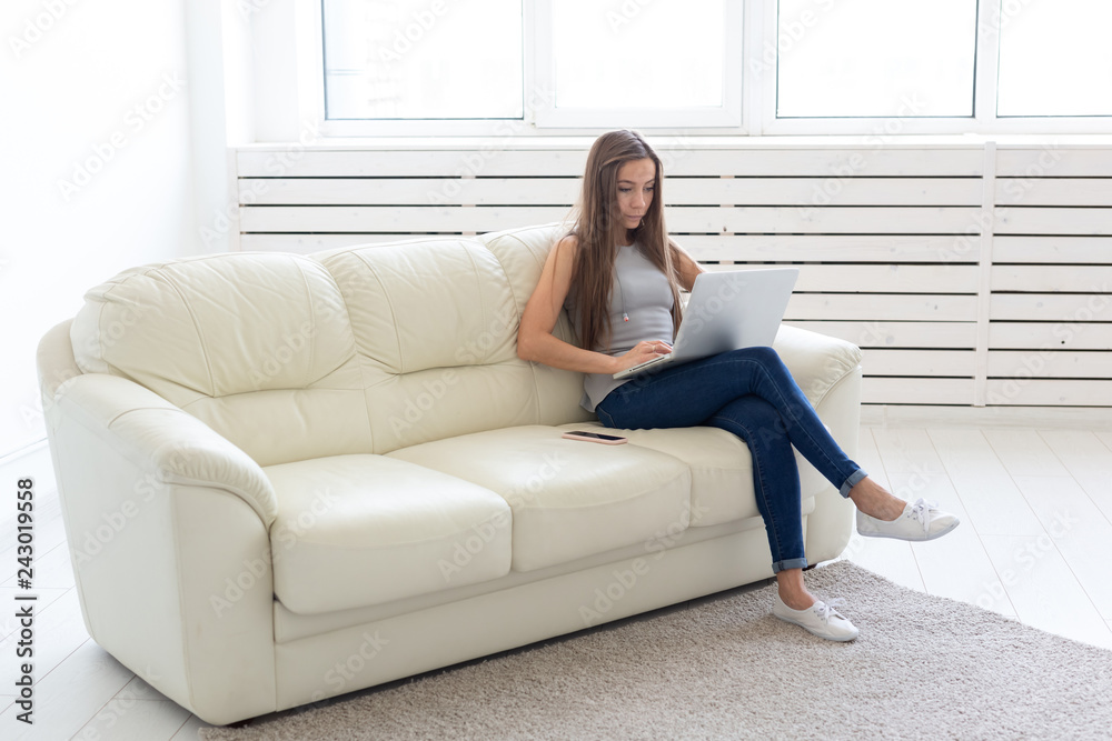 Technologies, freelance and people concept - young woman sitting on the white sofa and chatting in the netbook Technologies, freelance and people concept - young woman sitting on the white sofa and chatting in the netbook