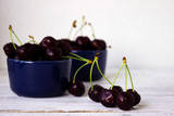 Ripe cherries in dark blue plates on wooden white background, he