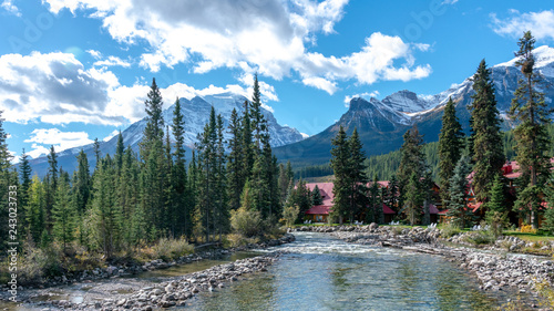 RUNNING CLEAR WATER STREAM IN PINE FOREST WITH HIGH ROCKY MOUNTAIN BACKGROUND IN BANF NATIONAL PARK  , ALBERTA , CANADA photo