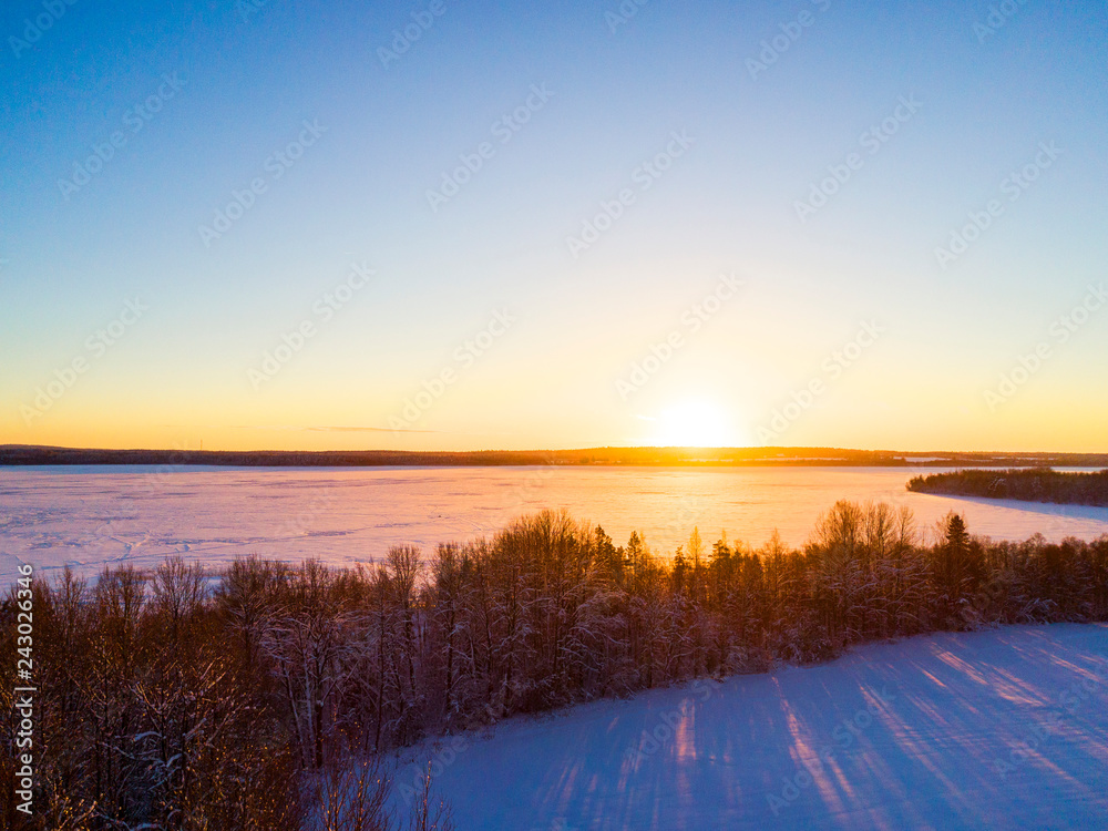 Aerial view of a gold sunset over winter snow-covered pine forest. Winter forest texture. Aerial drone view of a winter landscape. Snow covered forest. Dramatic gold sunset sky over frozen lake