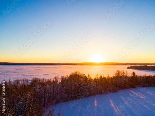Aerial view of a gold sunset over winter snow-covered pine forest. Winter forest texture. Aerial drone view of a winter landscape. Snow covered forest. Dramatic gold sunset sky over frozen lake