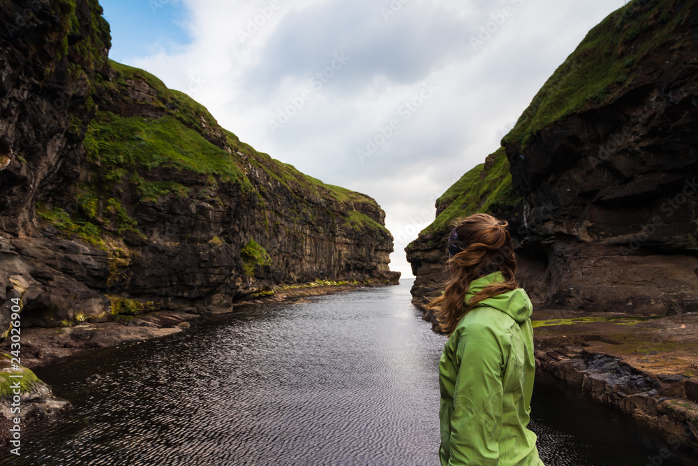 Woman looking out on the natural harbor in Gjogv, Faroe Islands, Denmark.