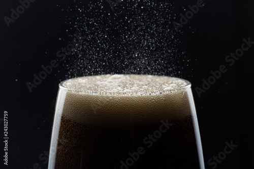 Glass of pouring fizzy drink with ice on a black background photo