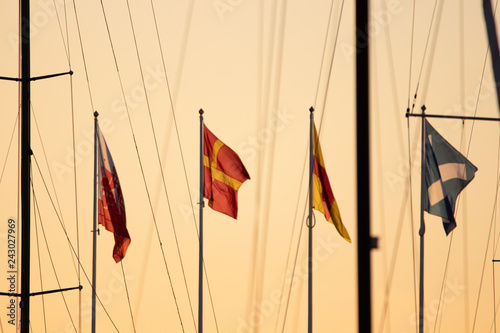 Flags blowing in the wind in a harbor in Helsingborg, Sweden during sunset. Skåne county flag.  photo