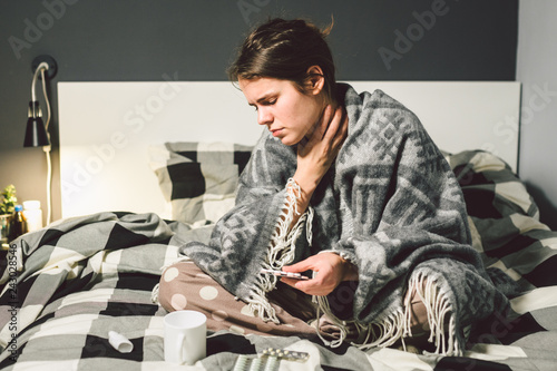 The topic is respiratory diseases and home remedies. Beautiful young woman is sick with a cold sitting in the bedroom on the bed holding her throat to shake the emotion. Sore throat man takes pills photo