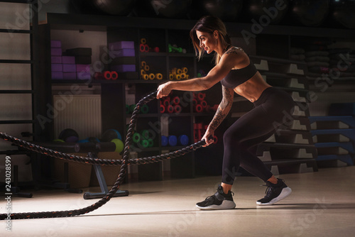 Strong woman exercising with battle ropes at the gym.