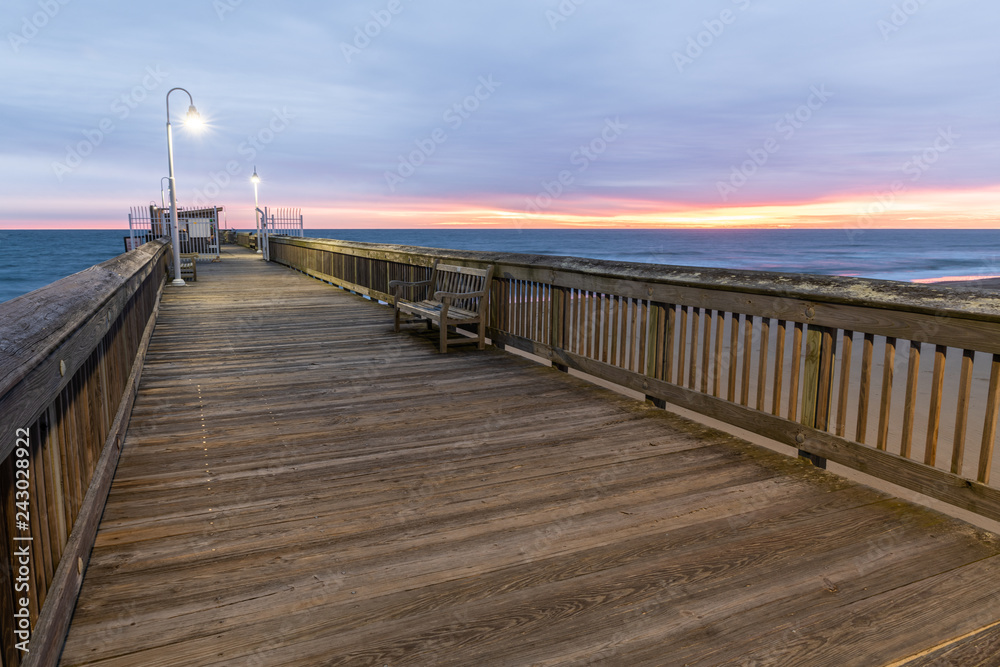 Sunrise from the Sandbridge Fishing Pier on Little Island Park in Virginia Beach.  The wood of the pier is lit by early morning sun rising in the clouds, creating pink and purple light.