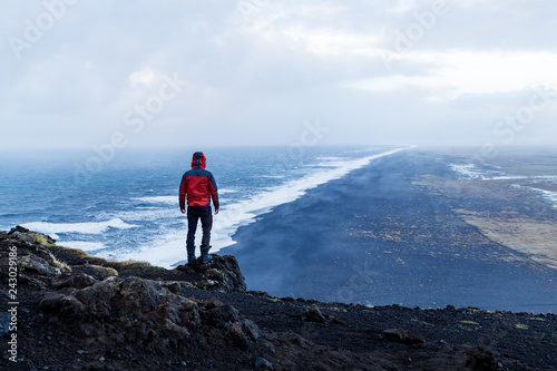 Person standing at Dyrholaey lighthouse in Iceland looking out over the black sand beach below during rain and harsh weather