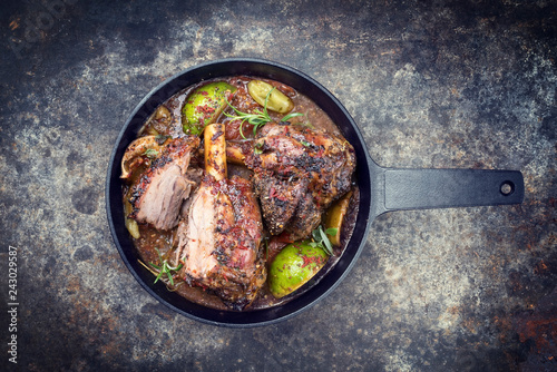 Traditional barbecue leg of lamb with lemon and tomatoes as top view in a cast-iron skillet with copy space