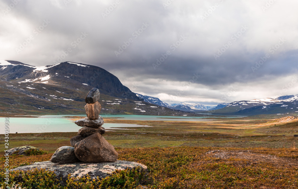 Stone formation showing the way at Kungsleden hike in northern Sweden. Sunrise, mountains and a lake during an early morning hike.  - obrazy, fototapety, plakaty 