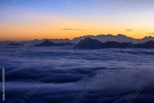 Sunset  Mountains and The Sea of Clouds - Snow Mountains in the distance protruding above a blanket of clouds like islands in an ocean - vibrant sunset sky  peaceful tranquility. Sunset above clouds