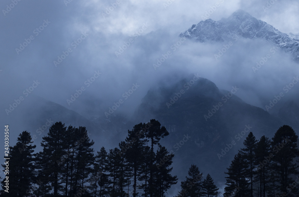 Clouds covering a mountain with trees below. Early morning in Nepal hiking Everest Base Camp Trek