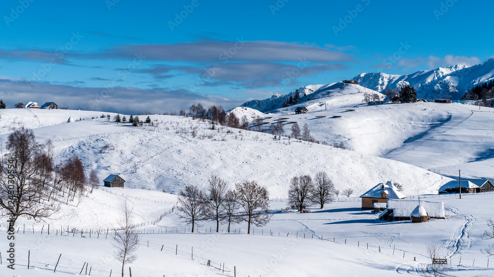 Mountain lodge in the picturesque Romania`s country side on a cold winter morning. Pristine clear ski  and snowy mountain peaks in the background. Piatra Craiului National Park.