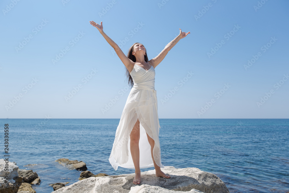 Girl in wedding dress posing against sea with arms outstretched Girl in wedding dress posing against sea with arms outstretched