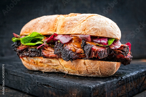 Traditional barbecue pulled pork piece of Bosten butt as sandwich with lettuce as closeup on a black board