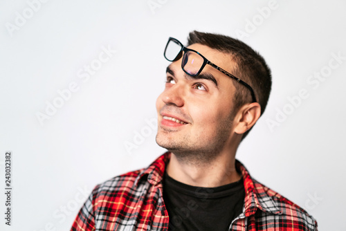 Happy young guy with his eyeglasses on forehead looking up isolated on white background. Portrait of smiling man taking trendy glasses off. © Vadim