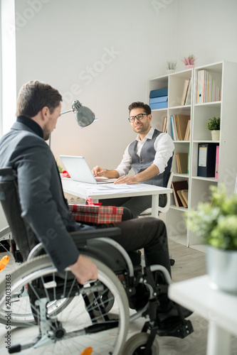 Disabled businessman sitting in wheelchair and moving to his colleague's table he is going to congratulate him with Christmas