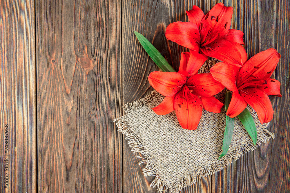 Red lilies with red ribbon and white paper blank on dark wooden background. Holidays card. Red lilies with red ribbon and white paper blank on dark wooden background. Holidays card.