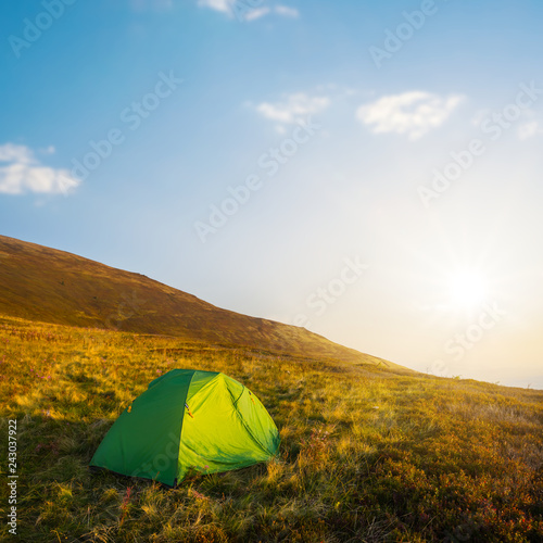 green touristic tent on a hill slope at the sunset
