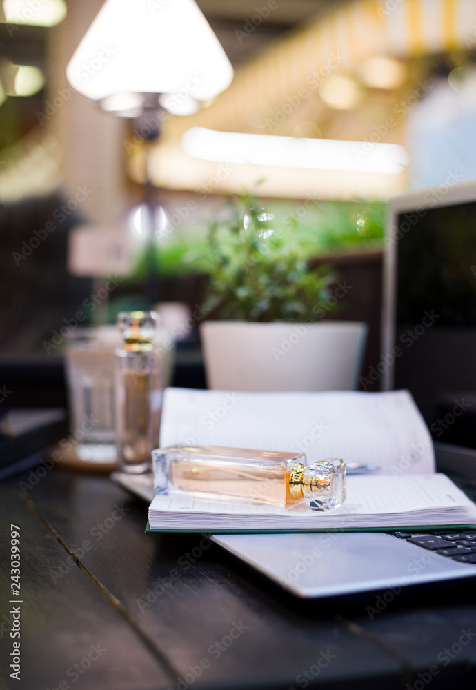 perfume lies on the surface of the notebook and laptop, perfume packaging on a wooden background, perfume on the background of the lamp and plants in the pot