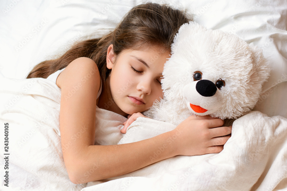 Cute little girl with long hair sleeping with teddy bear in bed. Adorable small child lies on warm comfortable bed having good dreams embracing her favourite soft toy at night Cute little girl with long hair sleeping with teddy bear in bed. Adorable small child lies on warm comfortable bed having good dreams embracing her favourite soft toy at night