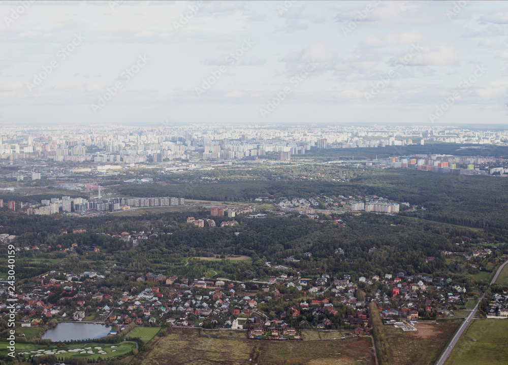 view from the window of the aircraft at dawn over the city, fields, forests, houses, shadows from the clouds, beautiful views of residential areas with houses, forest strips (horizontally)