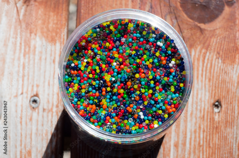 Dehydrated multicolored water beads in plastic jar on wooden deck