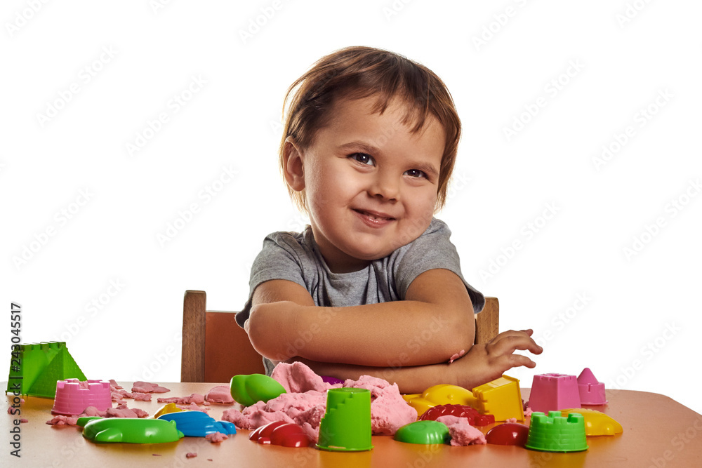 Little child girl is playing with green kinetic sand on the brown table; selective focus Little child girl is playing with green kinetic sand on the brown table; selective focus
