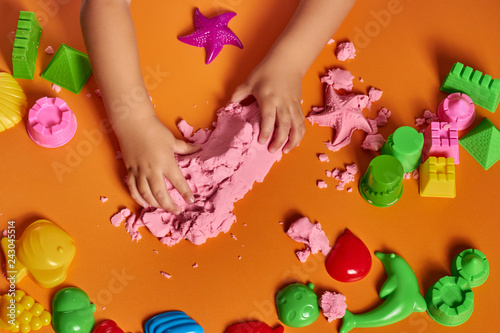 The hands of a child playing with kinetic sand. Close up. Orange background