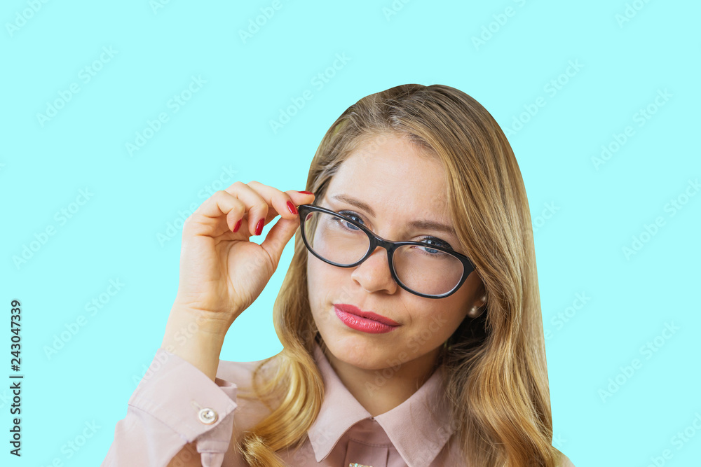 Portrait of a young attractive blonde in glasses who holds glasses with lowered eyes looking through them into the camera with a serious view on an isolated background, emotions Portrait of a young attractive blonde in glasses who holds glasses with lowered eyes looking through them into the camera with a serious view on an isolated background, emotions