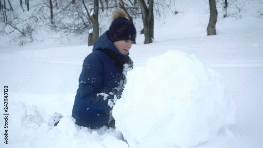 boy rolls big snow ball for snowman in winter. boy rolls big snow ball for snowman in winter.