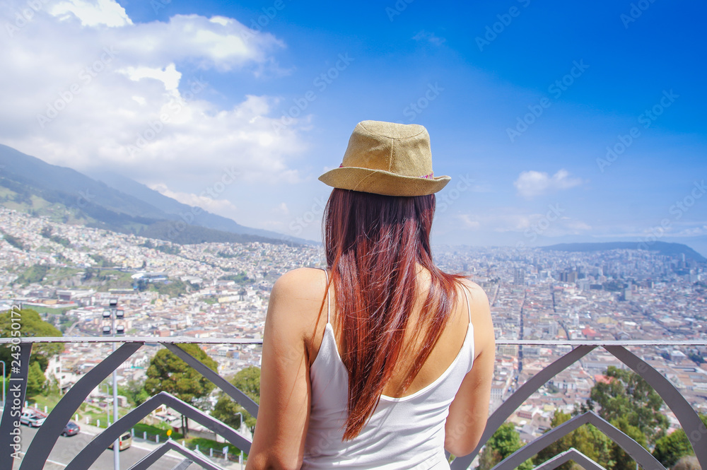 Fototapeta premium Back view of young woman wearing a panama hat and enjoying the panoramic view from el Panecillo on the historical centre of Quito