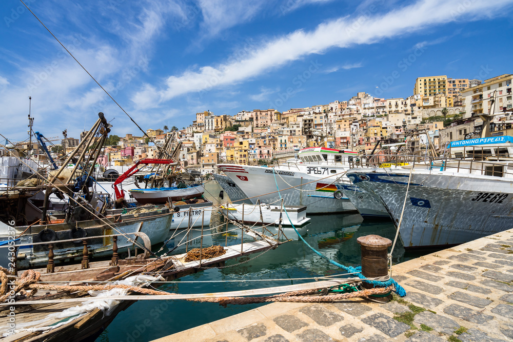 Fishing boats moored at Sciacca harbour with the colorful old town buildings on the background, Sicily, Italy
