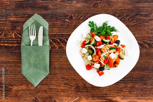 Greek salad of fresh cucumber, tomato, sweet pepper, lettuce, red onion, feta cheese and olives with olive oil. Healthy food, top view with appliances