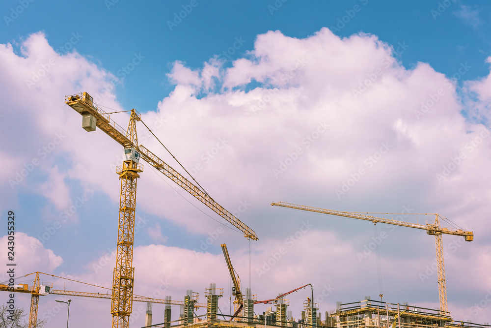 Construction tower cranes against the blue sky with clouds Construction tower cranes against the blue sky with clouds
