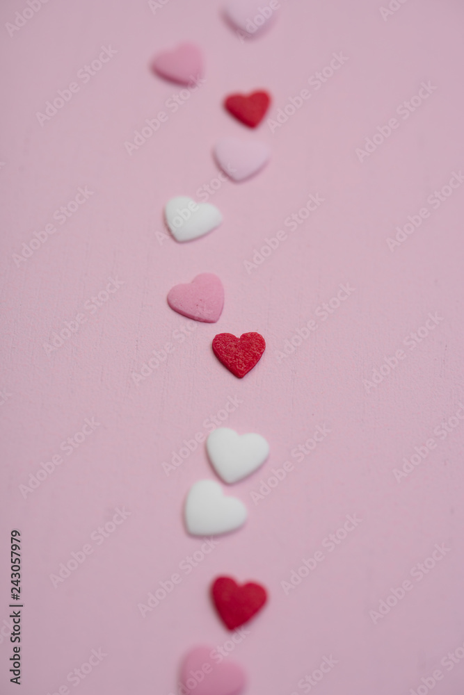 Flatlay with tiny heart-shaped sugar sprinkles in red, white and pink laid out in trace of trail as card for Valentine's Day on February 14th on wooden background, symbol of love and romantic feeling