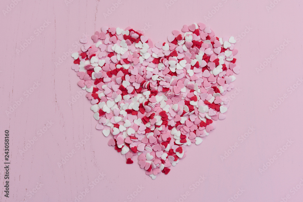 Top view flat lay with huge heart made of hundreds of small red, white and pink heart-shaped sweet sugar cupcake sprinkles as symbol for romantic love on wooden background for Valentine's Day card