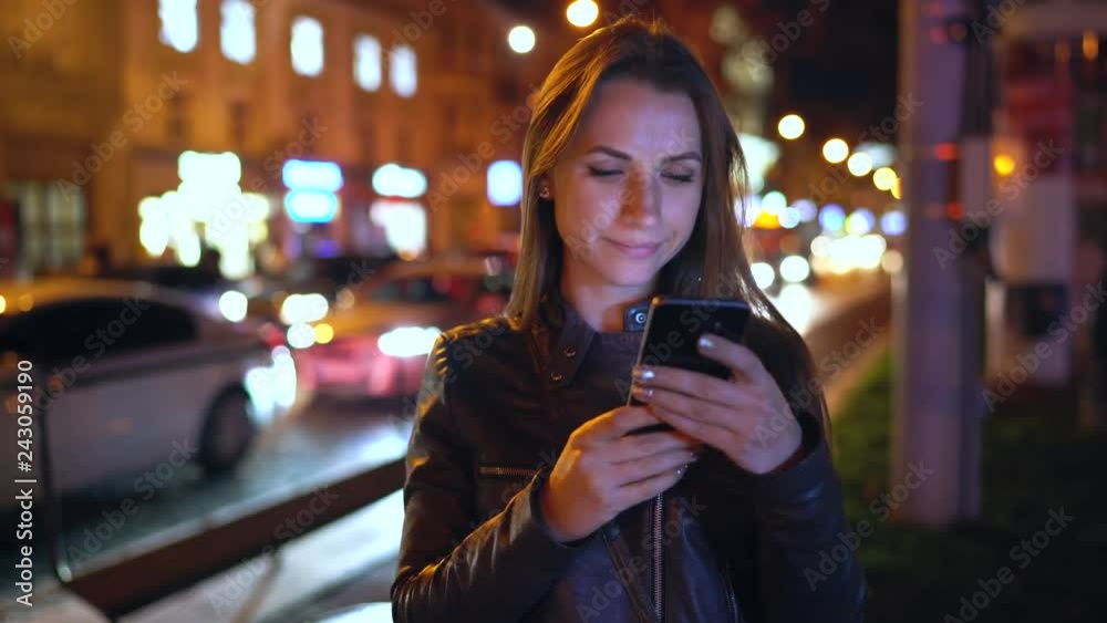 Attractive woman using a smartphone while walking through the streets of the evening city