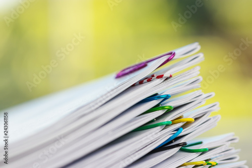 Close up pile of unfinished homework assignment stacked in archive with colorful paper clips on table in school waiting to be managed and inspected. Stack of paperwork. Education and business concept.
