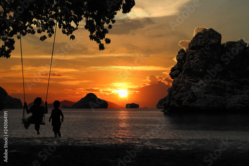 Silhouette of mother and son sitting on cradle or hammock on the beach with red sky sunset