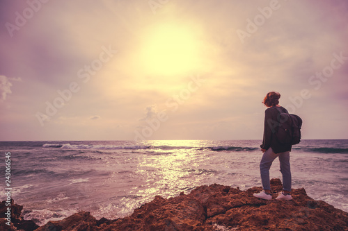 A girl with a backpack is standing with her back on the stormy seashore, an image with retro toning