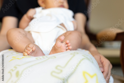 Baby feet resting on mother lap in the house.